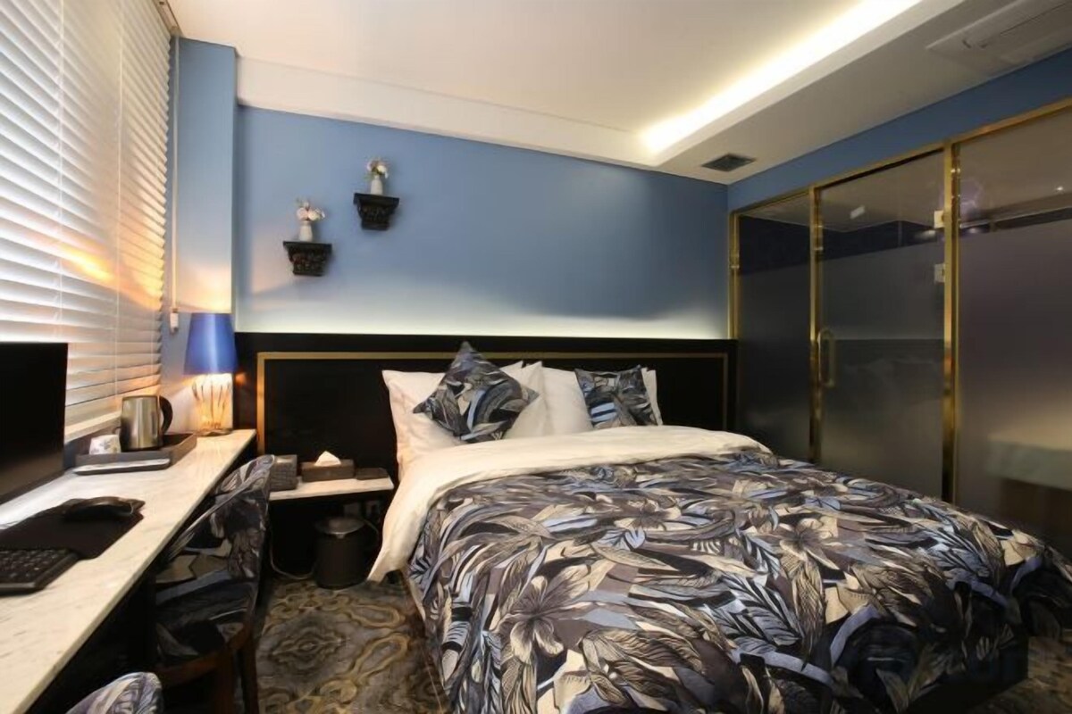 Una habitación de hotel con una cama, un escritorio, una silla, una mesita de noche y un armario.