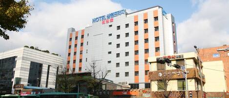 Un hotel a più piani con un cartello ben visibile, circondato da negozi e veicoli sulla strada.