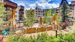 A hotel courtyard with a playground, outdoor seating, and a mountain backdrop. - Lift House Lodge (Vail)