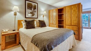 A bedroom with a bed, two bedside lamps, a telephone, a framed picture, and a wooden wardrobe. - Lift House Lodge (Vail)