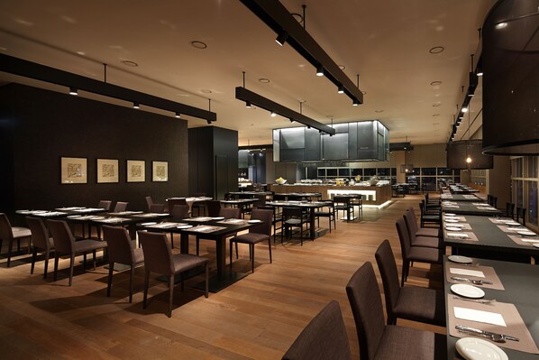 Un restaurante moderno con una barra larga, varias mesas y una zona de cocina central.