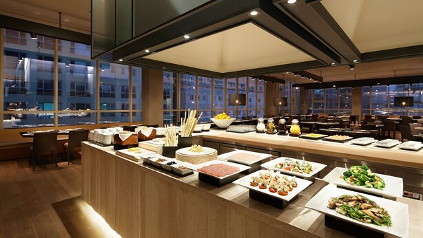 A buffet with various food items and a view of the cityscape through large windows. - Shilla Stay Dongtan (Hwaseong)