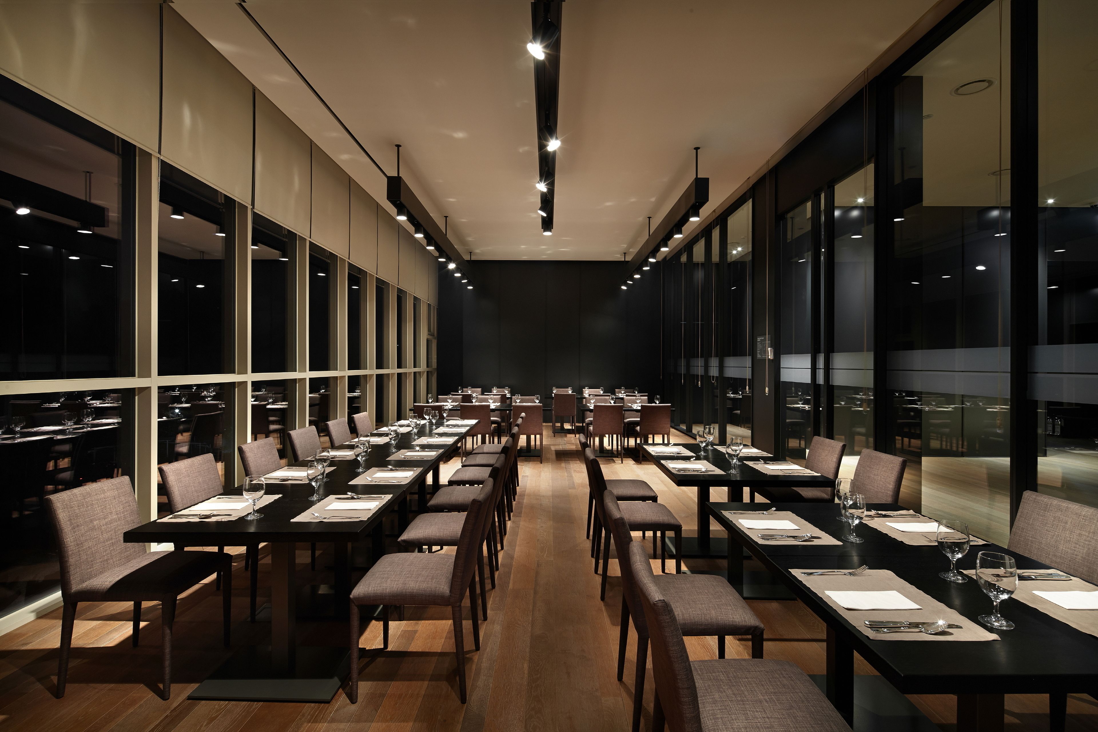 A spacious dining area with long tables and chairs, large windows, and modern lighting.