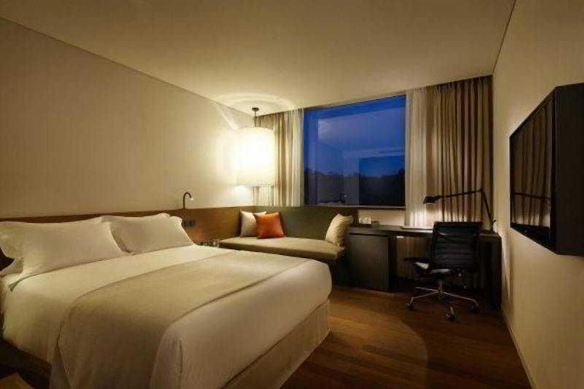 A hotel room with a large bed, a desk, a chair, and a window with curtains.