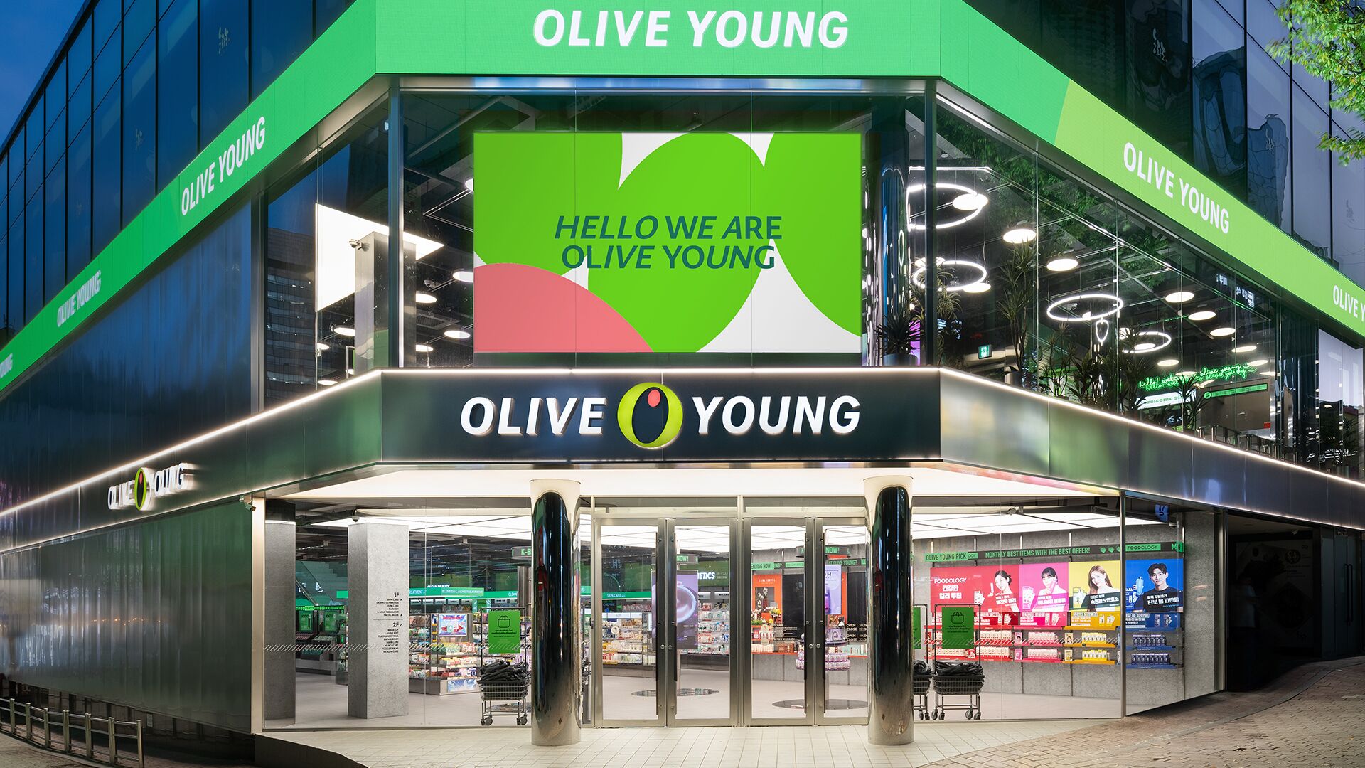The exterior of an Olive Young store with a large sign reading "Hello We Are Olive Young" and a logo featuring a green circle with a white olive.