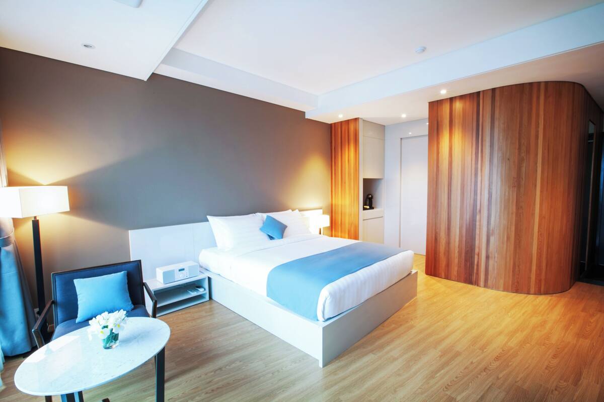 A modern hotel room with a bed, bedside table, lamp, and a small round table with flowers.