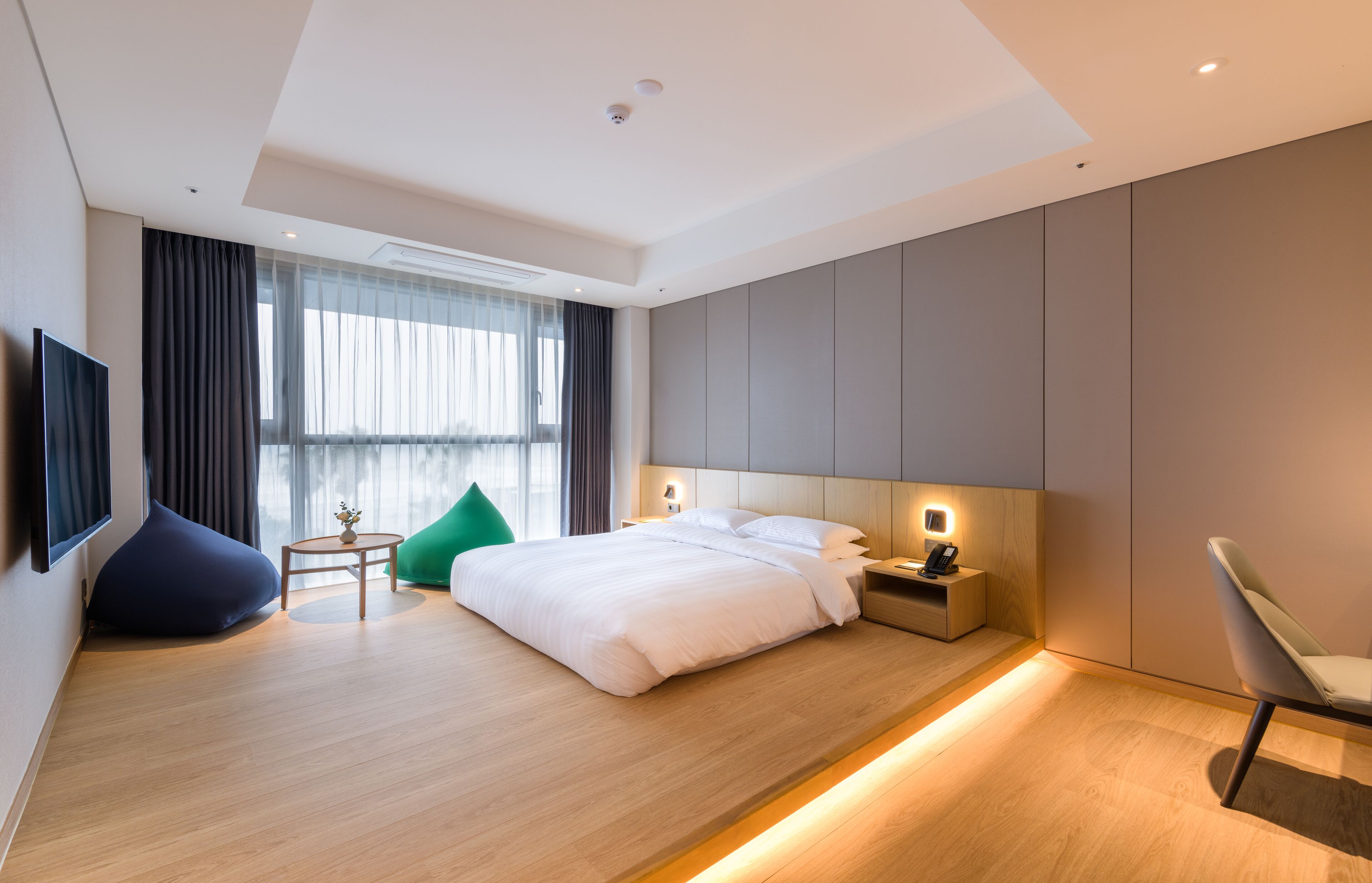 A modern hotel room with a large bed, bedside tables, a TV, and a view of the city.