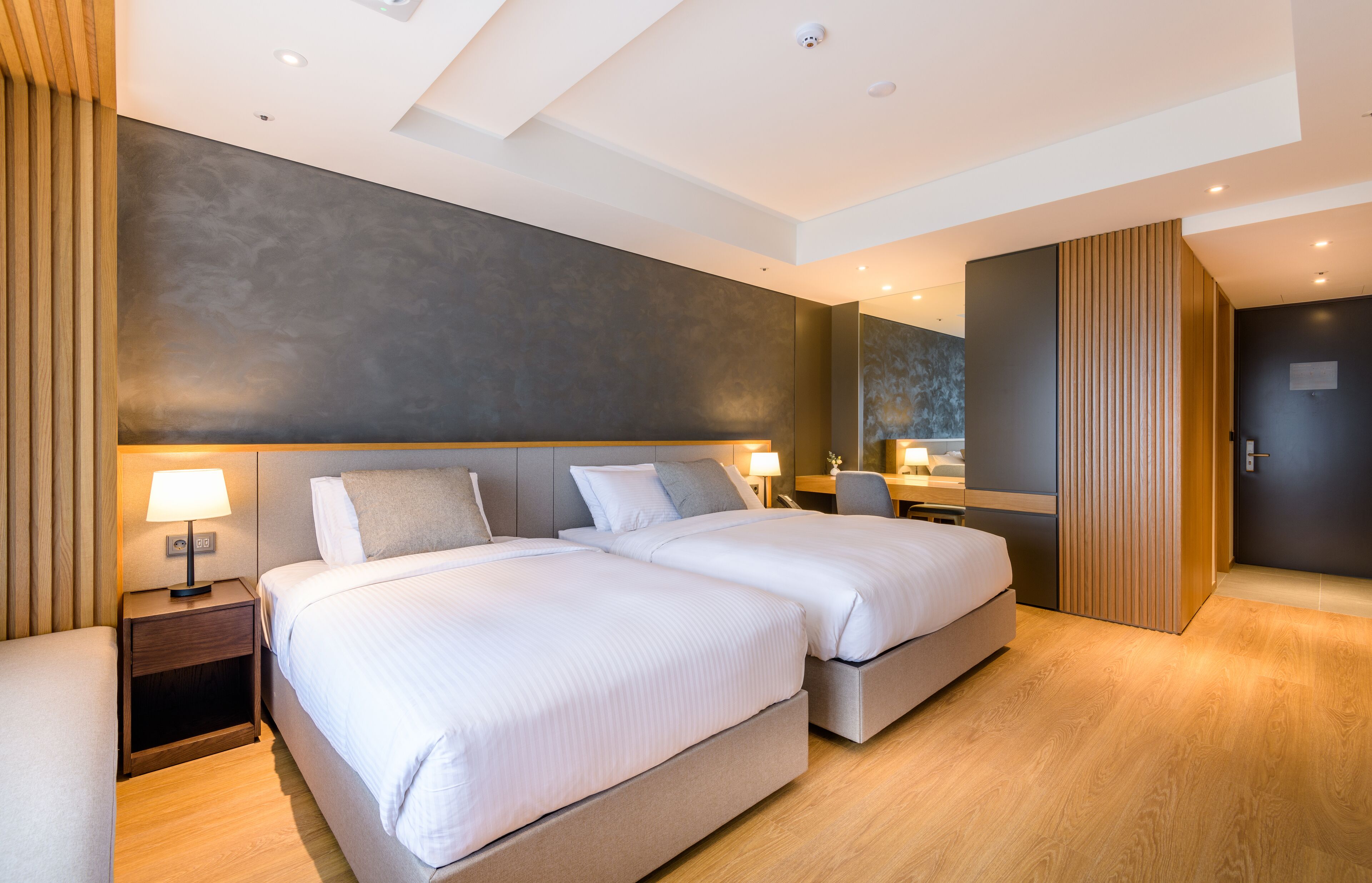 Ein modernes Hotelzimmer mit zwei Betten, einem Schreibtisch und einem großen Spiegel.