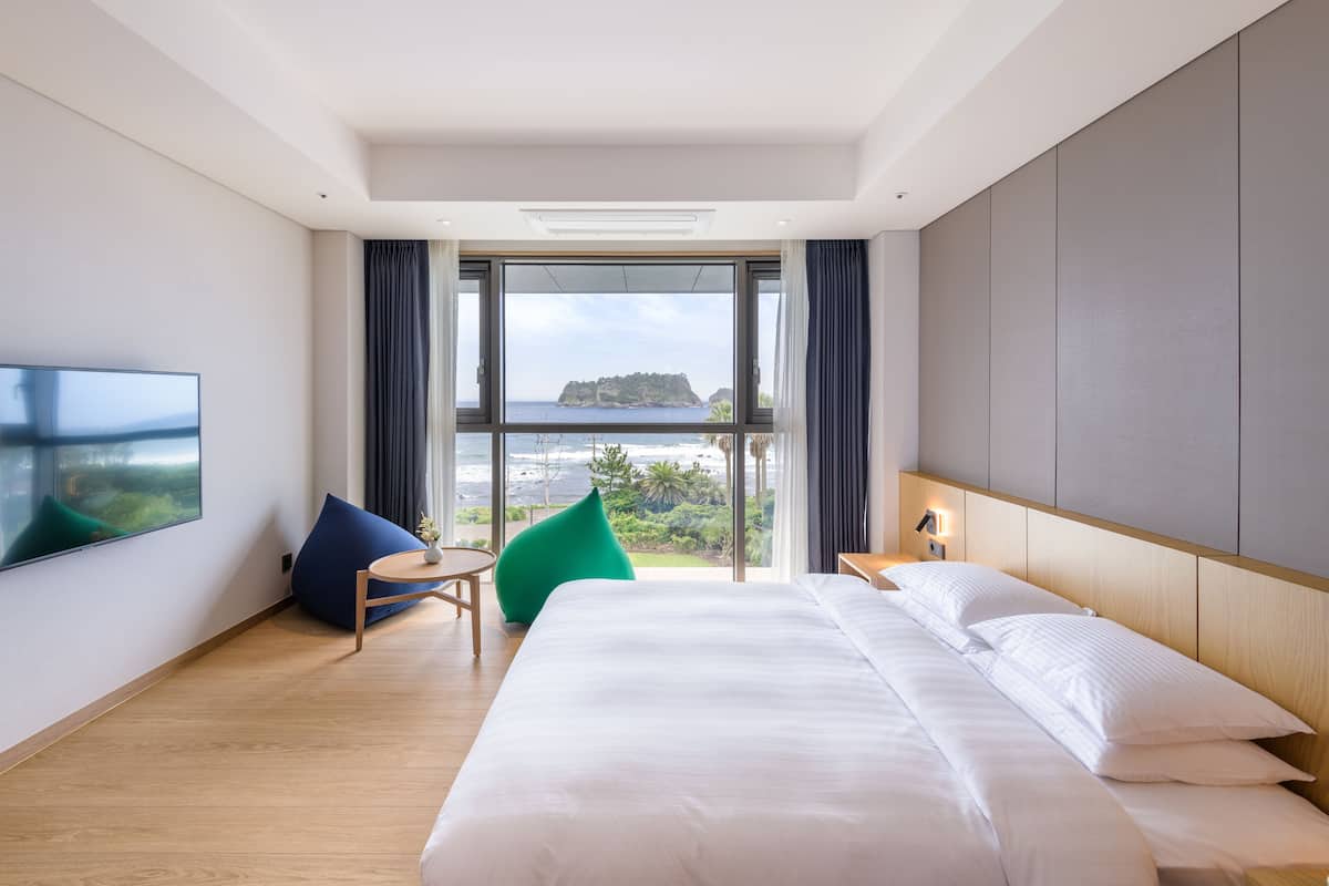 A hotel room with a large bed, a TV, a view of the sea, and a balcony.