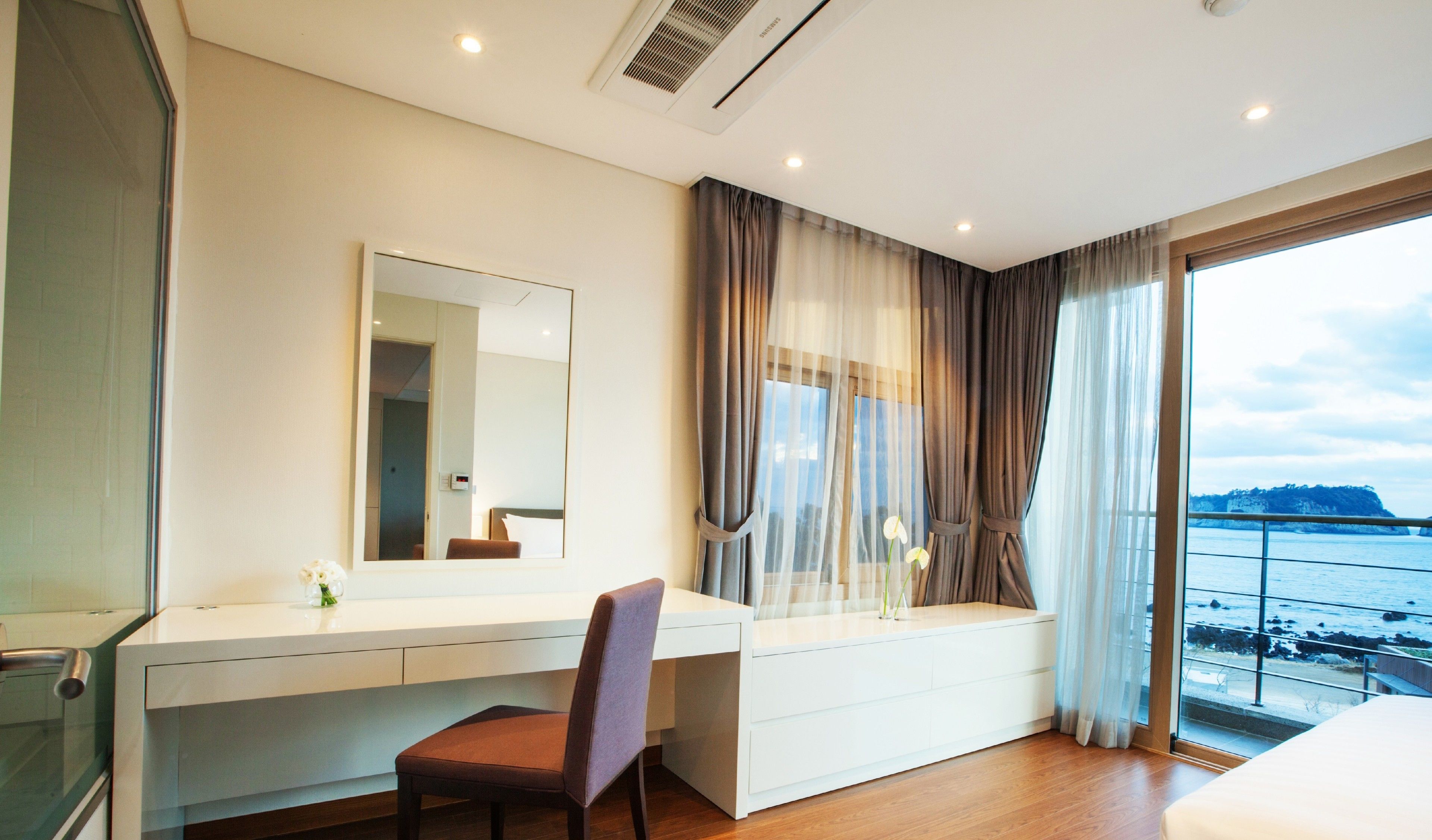 A modern hotel room with a large window, a desk, a chair, and a bed.