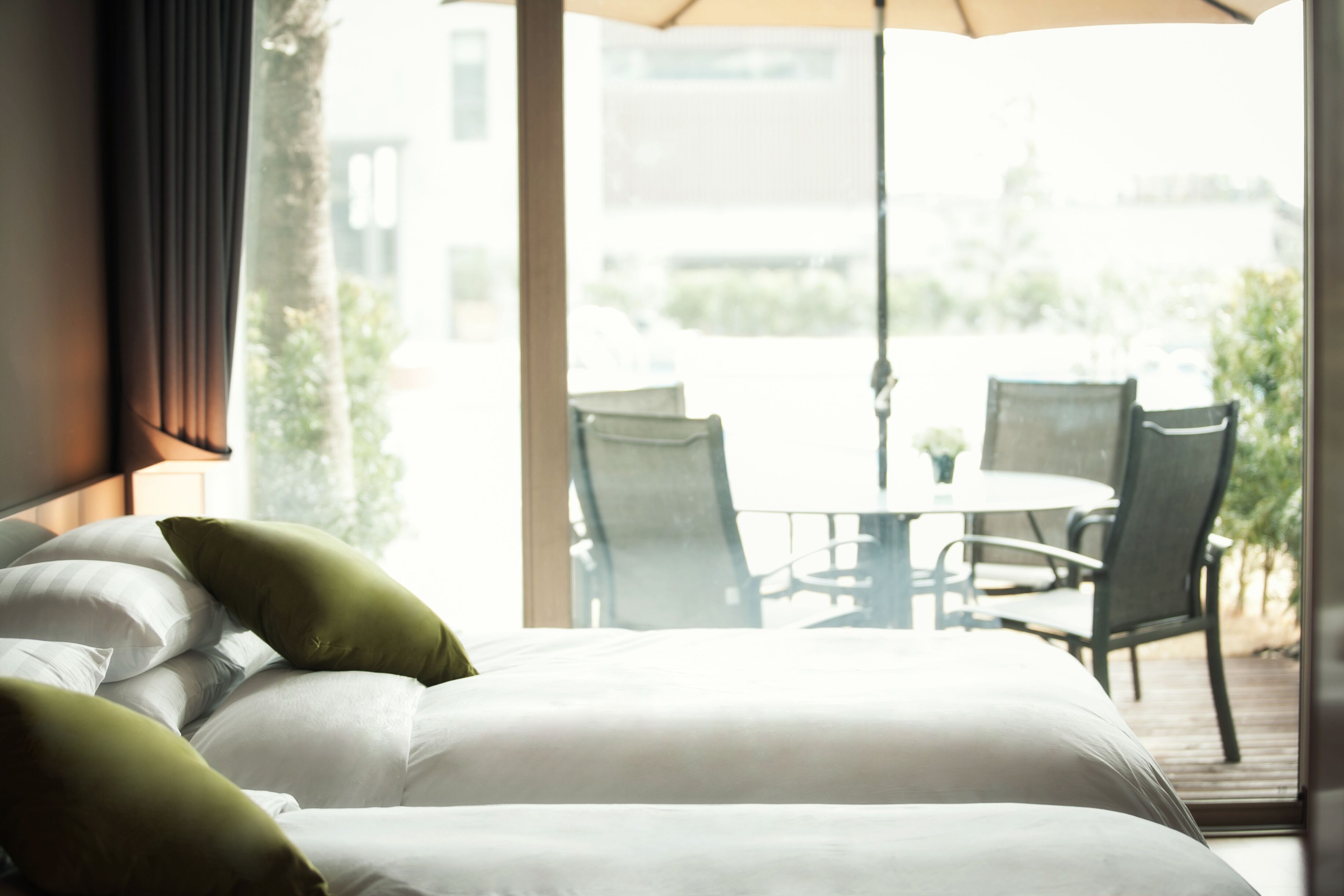 Habitación de hotel con cama, almohadas verdes y vista a un patio exterior con sillas y una mesa.