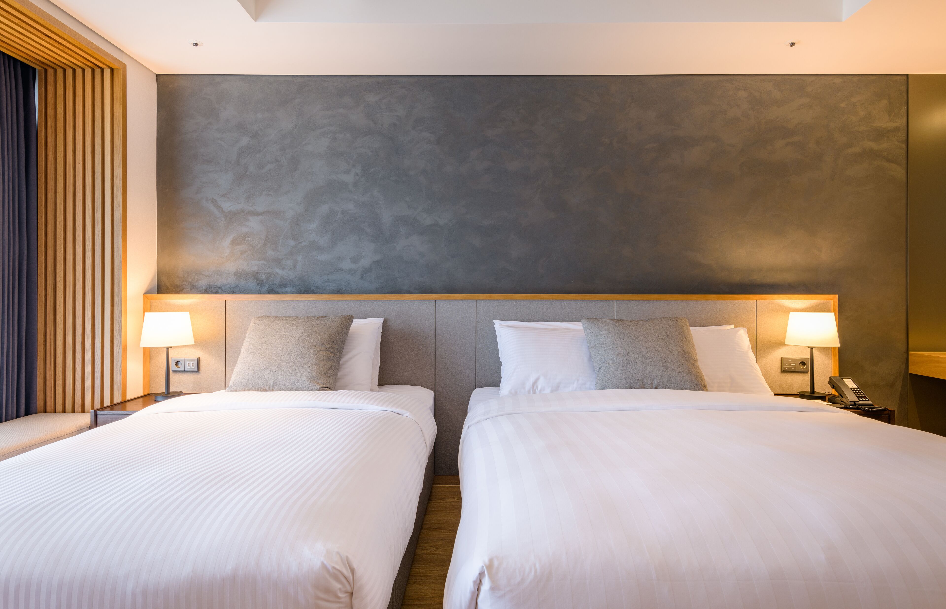 Une chambre d’hôtel avec deux lits, un grand mur à texture et des lampes de chevet.