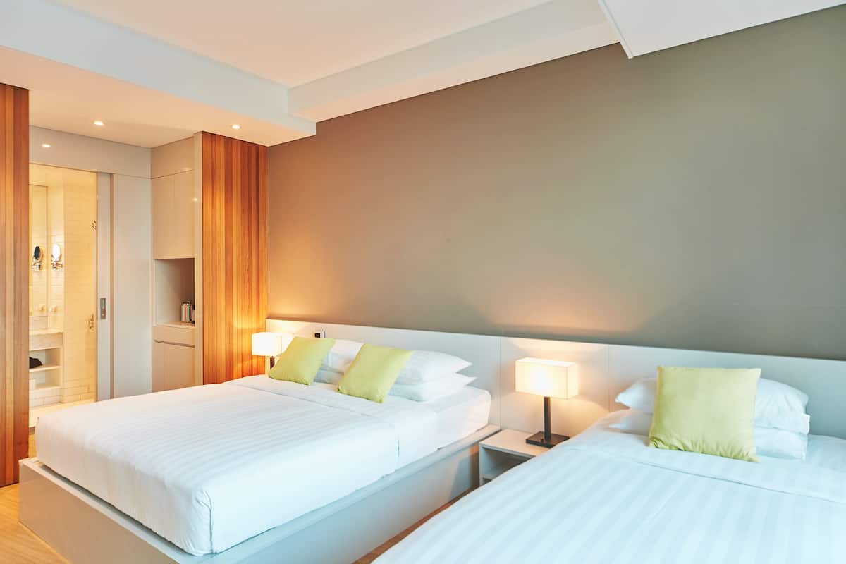 A hotel room with two beds, a wooden wardrobe, and a bathroom with a shower and toilet.