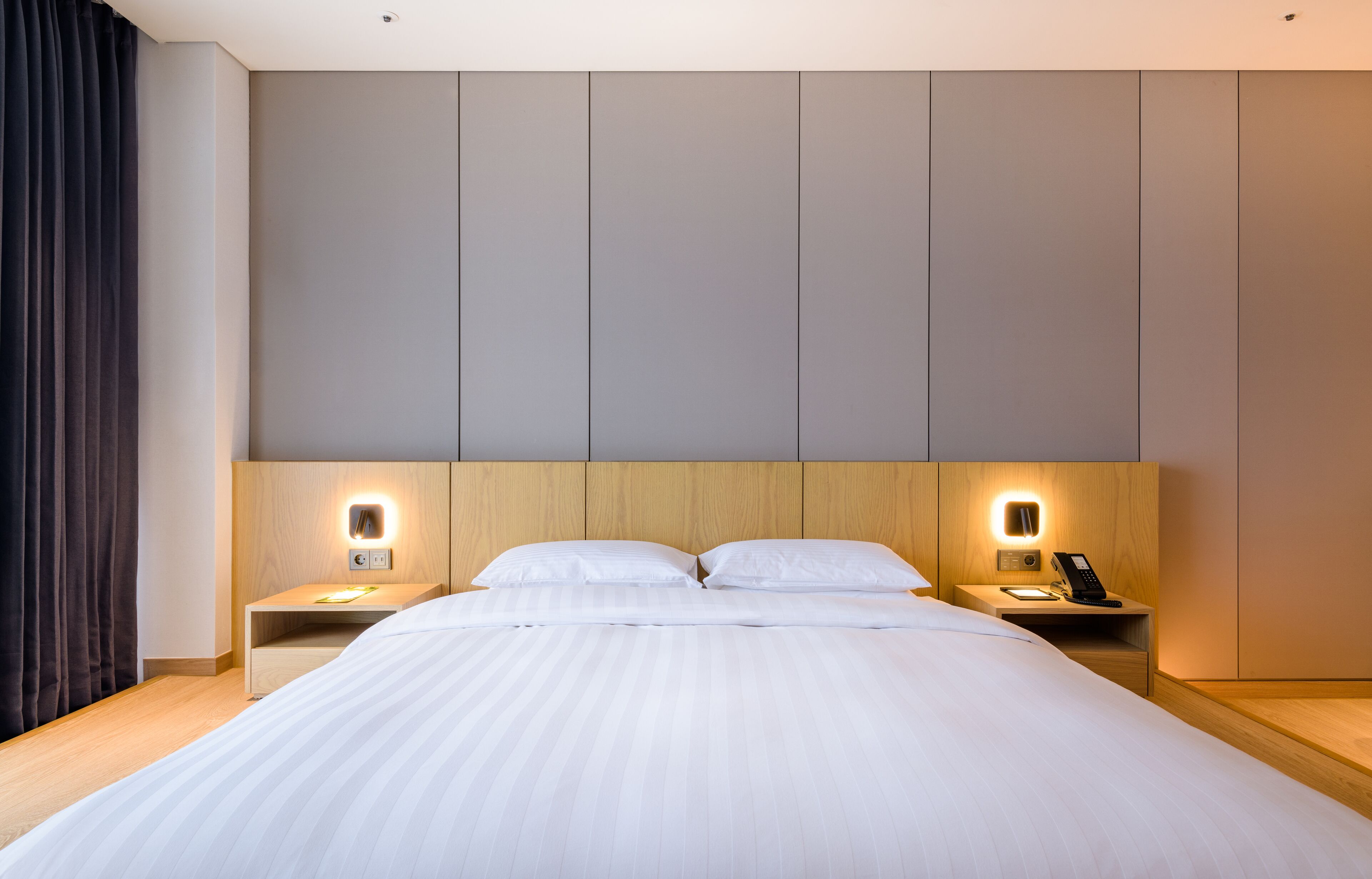 A modern hotel room with a large bed, two bedside tables with lamps, and a wooden headboard.