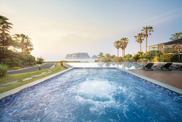A swimming pool with lounge chairs, palm trees, and a view of the sea.