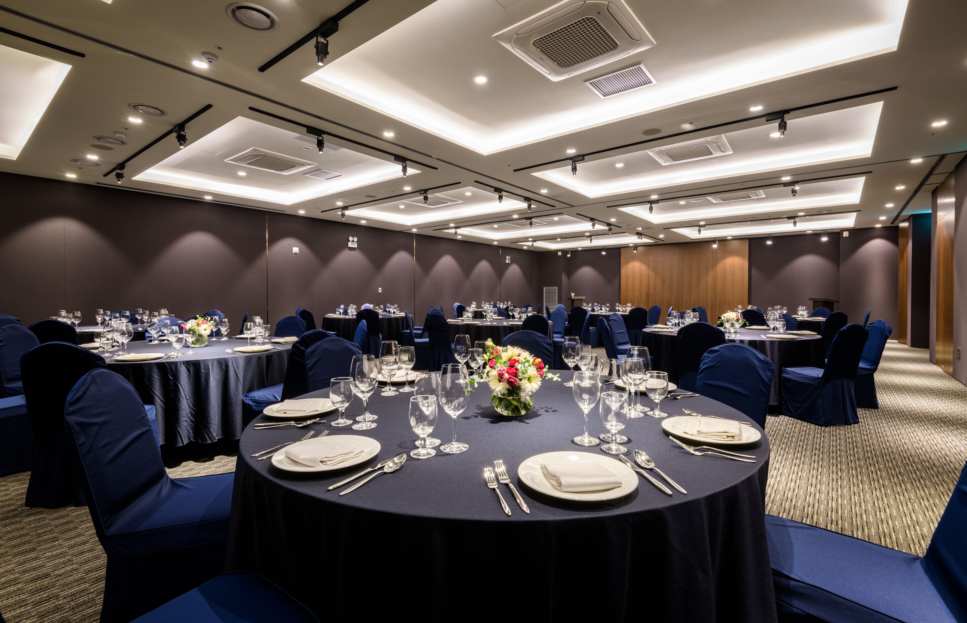 A conference room with round tables, blue chairs, and a dark tablecloth.