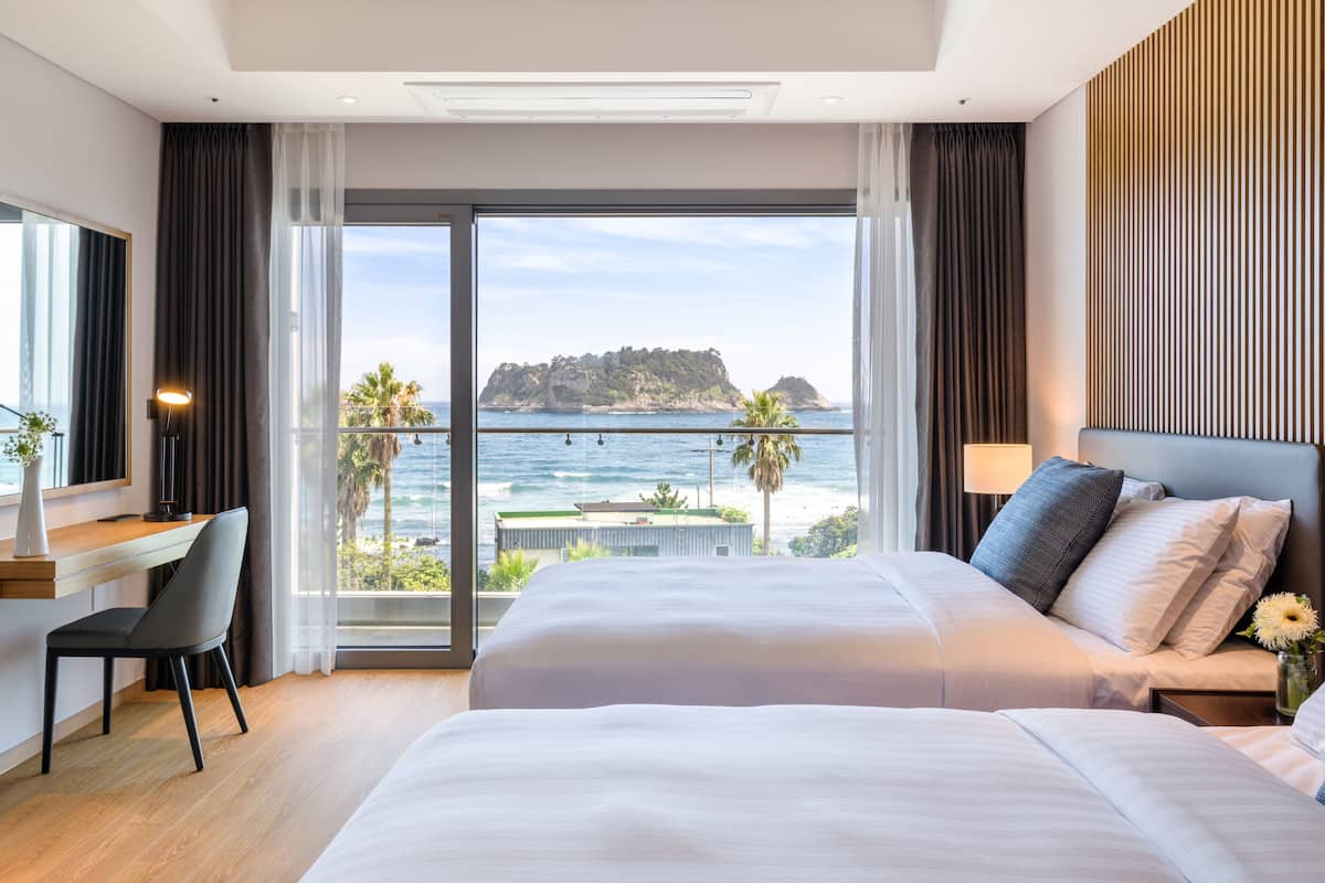 A modern hotel room with a large bed, a desk, and a view of the sea.
