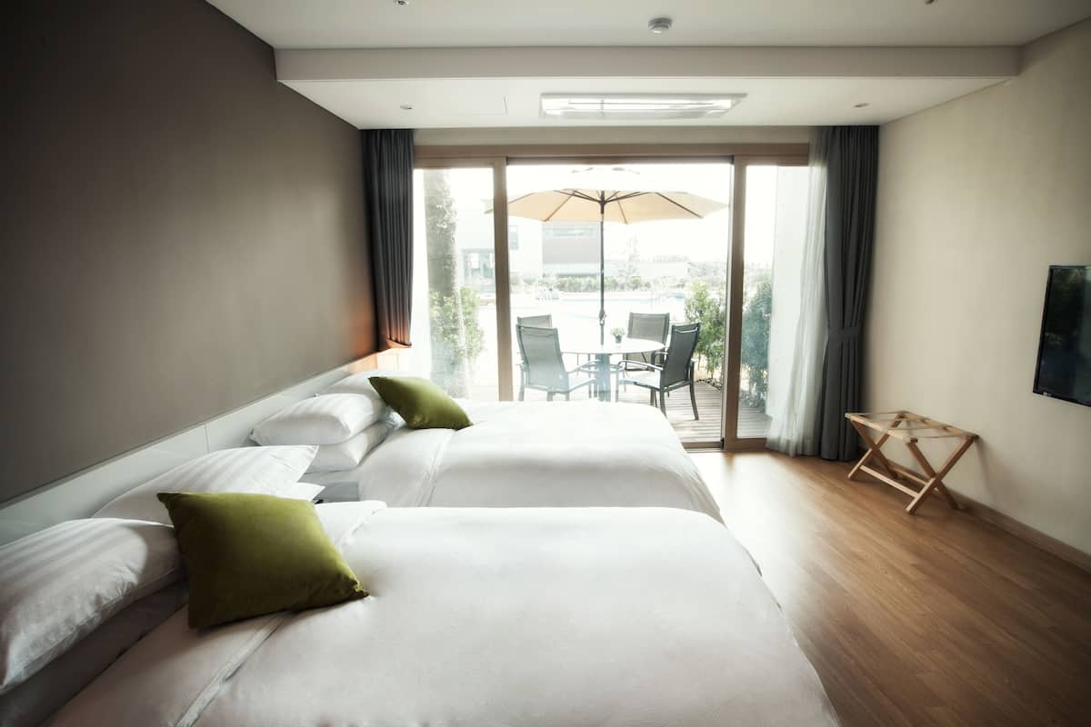A hotel room with a large bed, a small table, and a view of the outdoors.