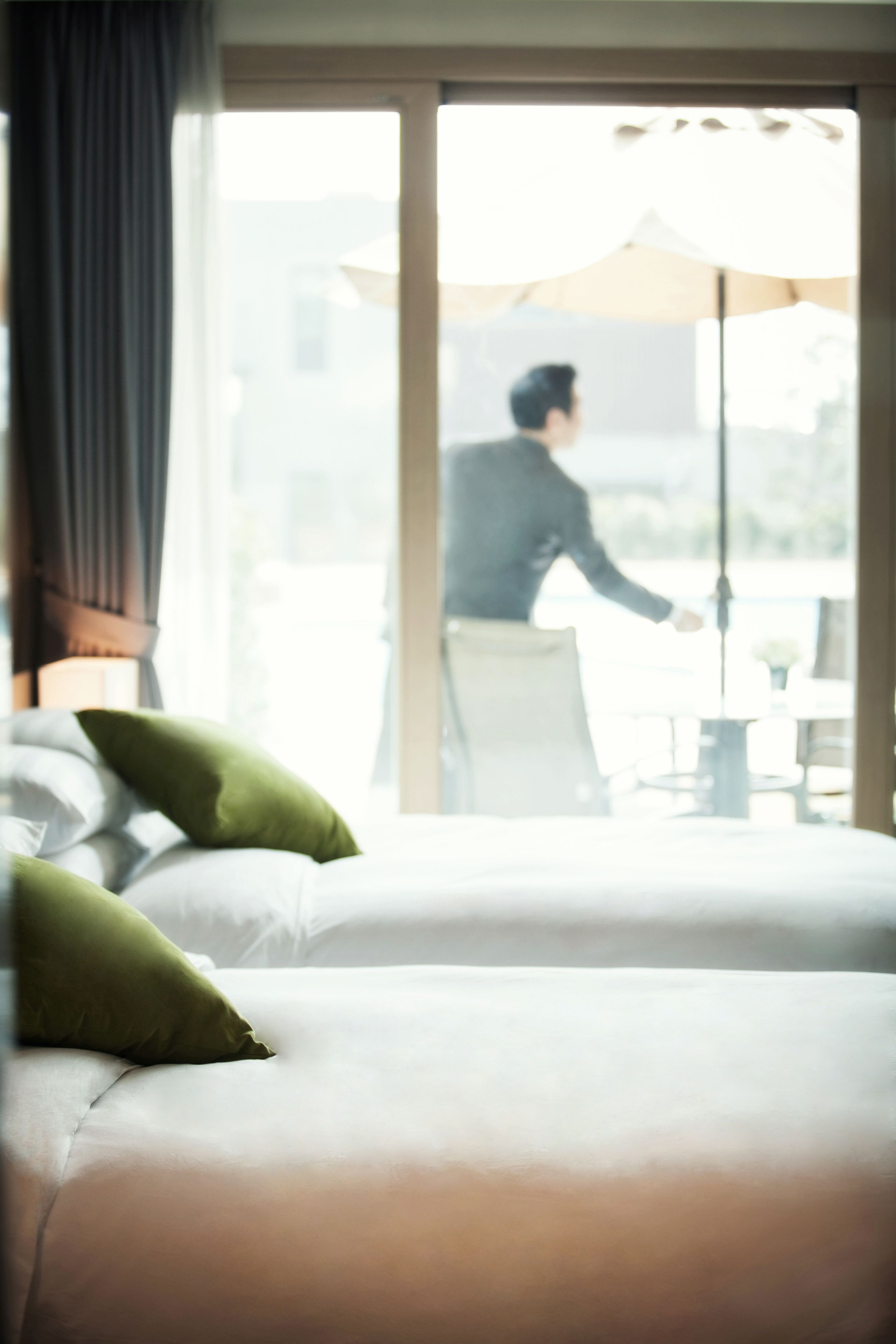 A hotel room with a bed, pillows, and a view of a person outside.