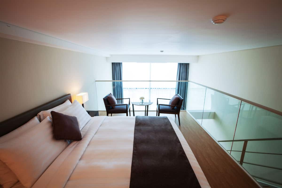 A hotel room with a bed, two chairs, a small table, and a balcony with a railing.