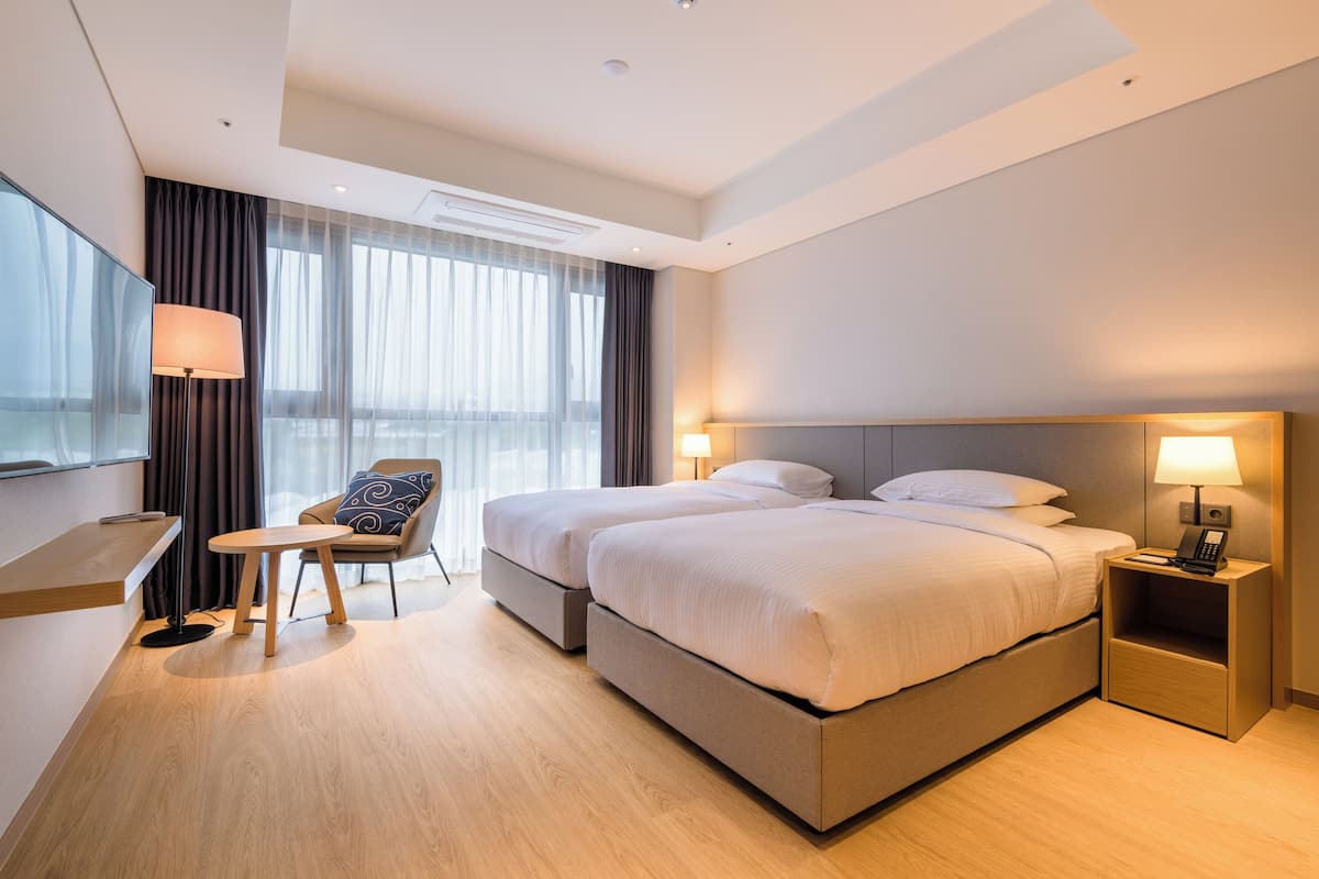 A modern hotel room with a large bed, a desk, a chair, and a TV.