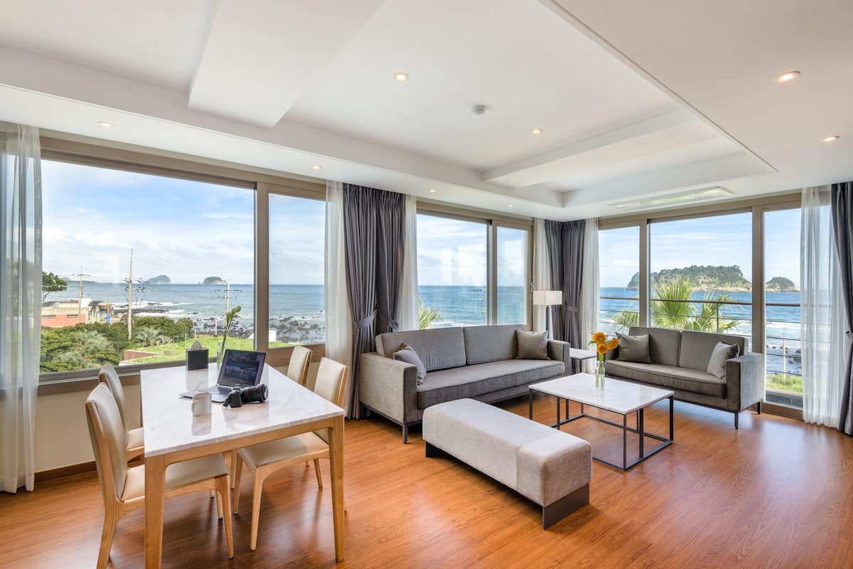 A spacious living room with a large window offering a view of the sea and a distant island.