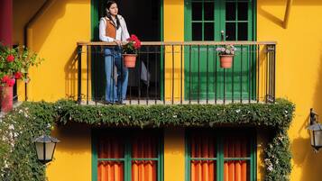 Un edificio amarillo con balcón, contraventanas verdes y plantas en macetas.