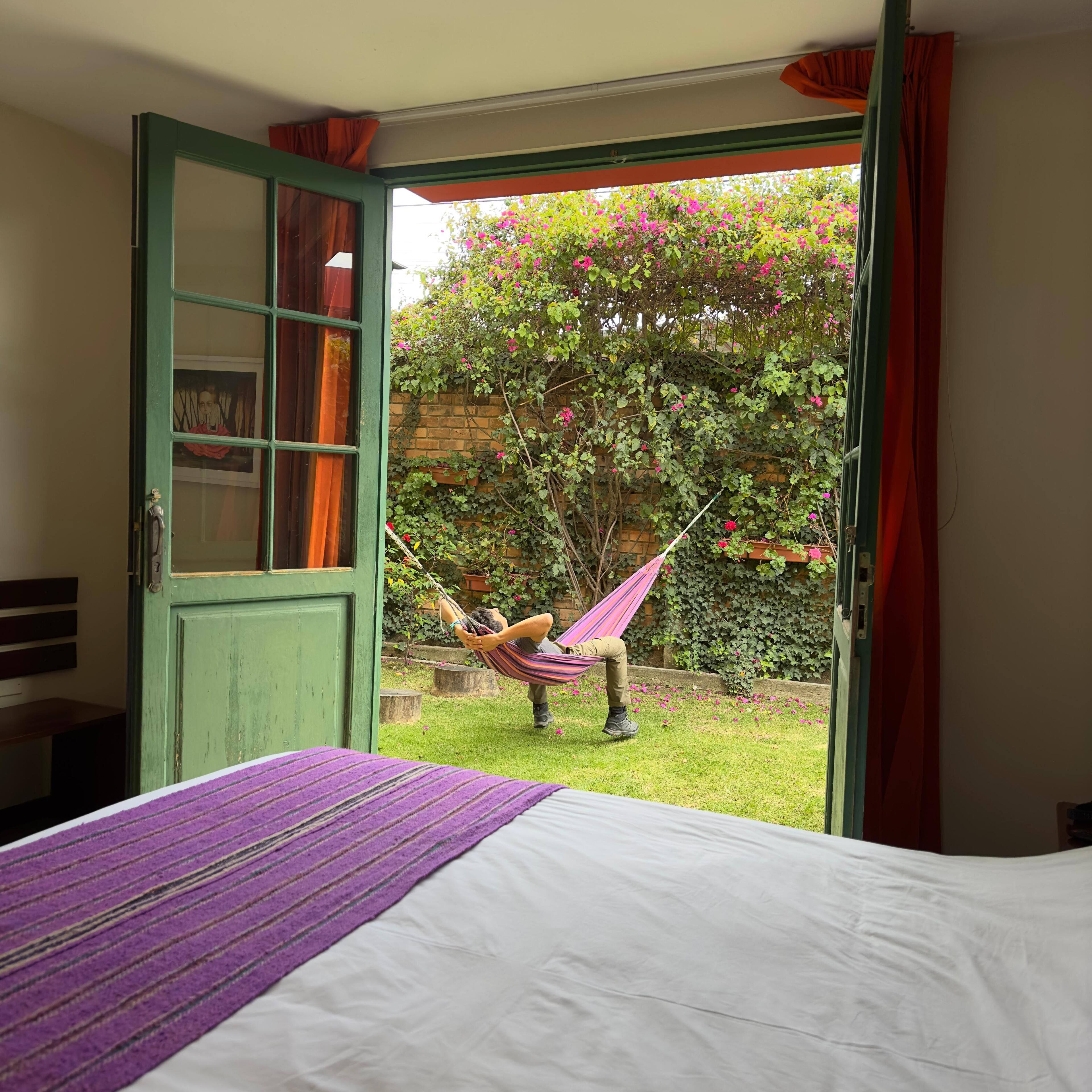 Quarto com uma cama, porta verde e vista para um jardim com rede.