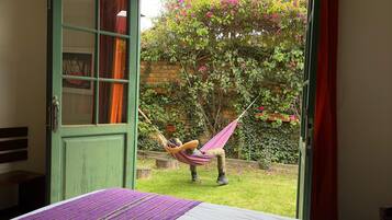Quarto com uma cama, porta verde e vista para um jardim com rede.