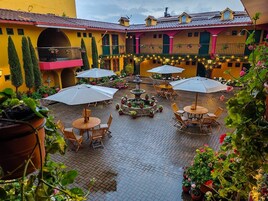 Un patio con mobiliario exterior, una fuente central y plantas en macetas.