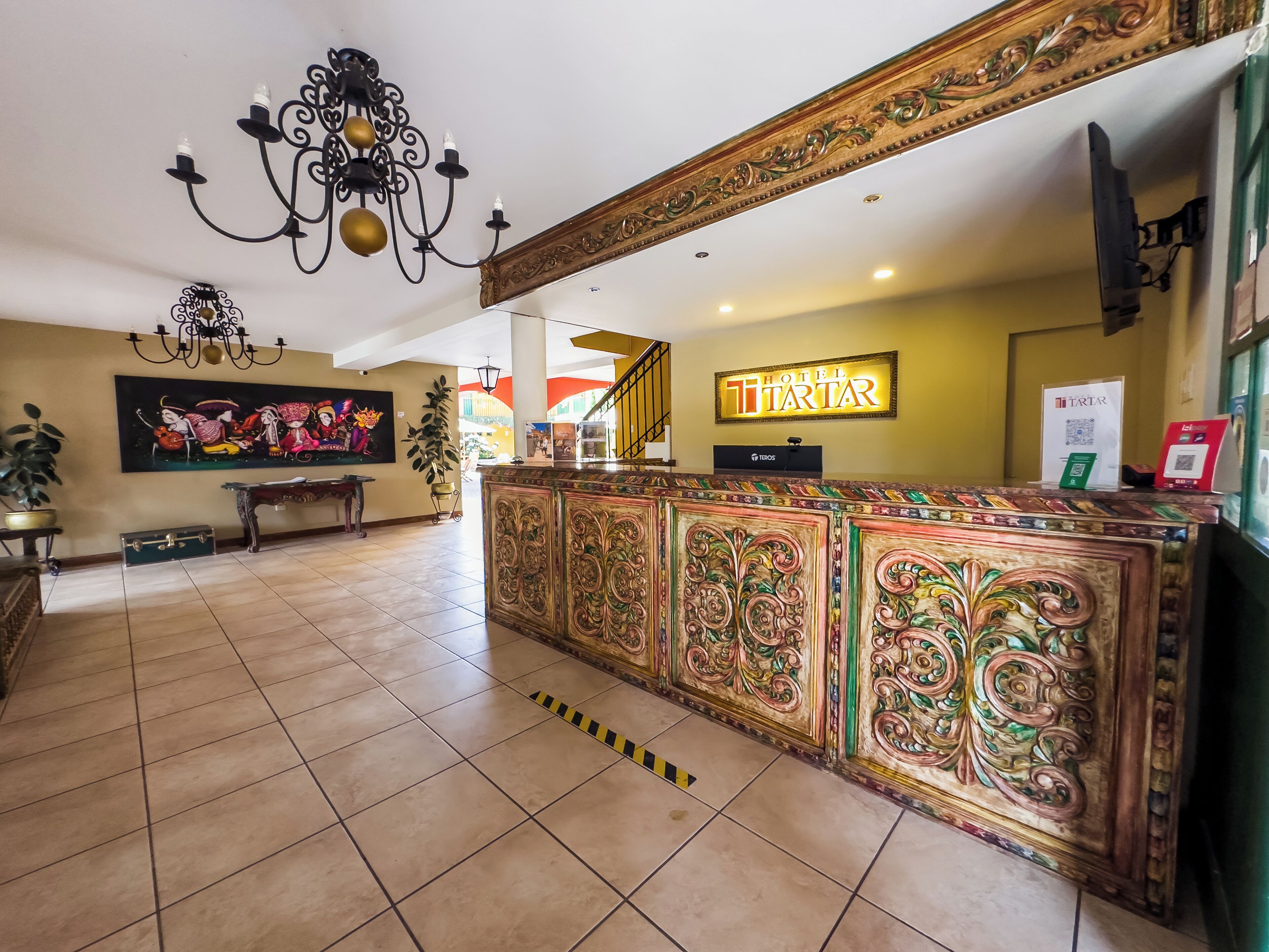Un vestíbulo de hotel con una recepción, una araña, un cuadro y una escalera.