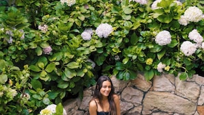 Een vrouw zittend op een stenen bank, omringd door weelderig groen en witte hortensia's.