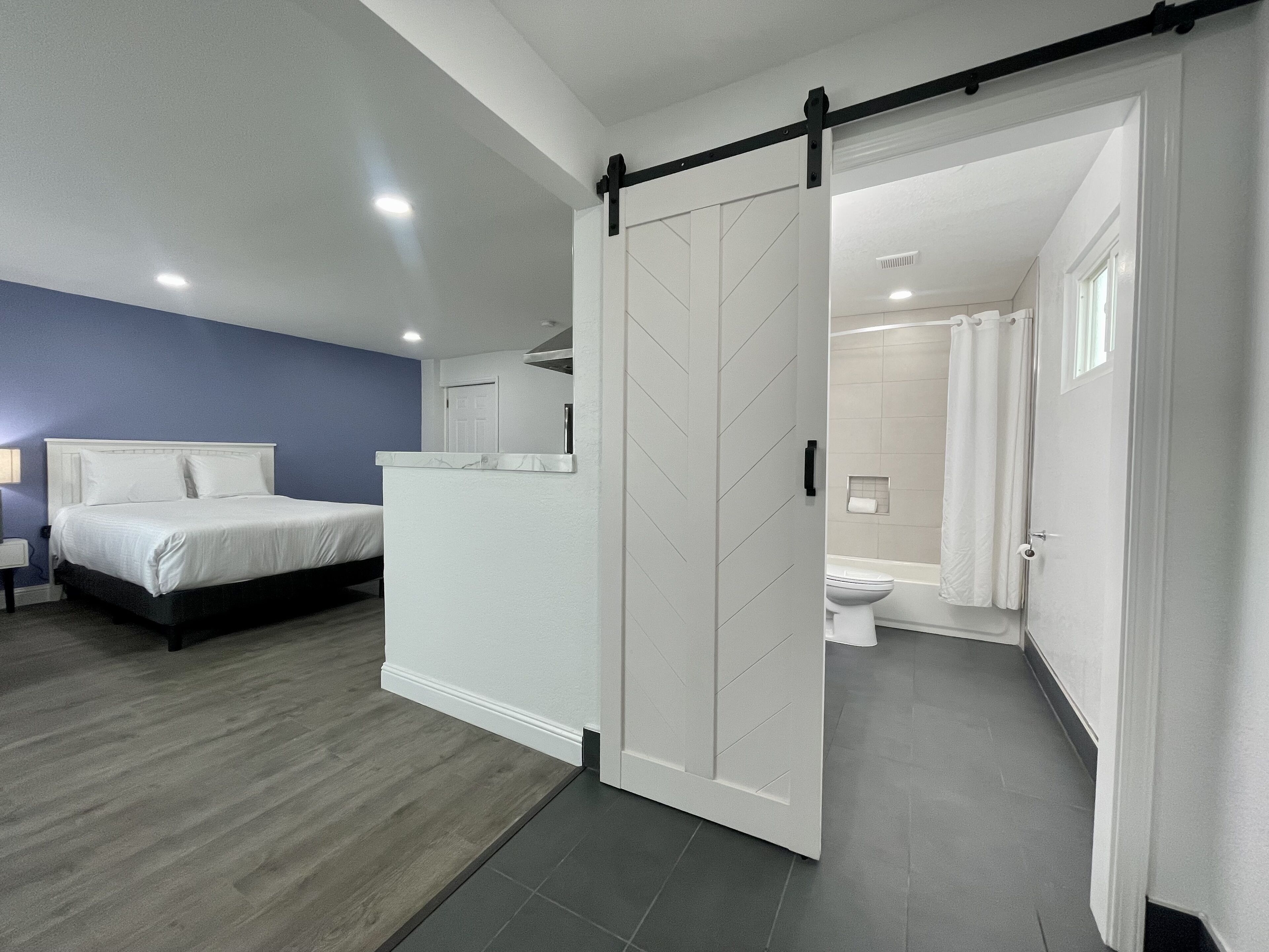 A modern bedroom with a bed, a bathroom with a toilet and shower, and a hallway.