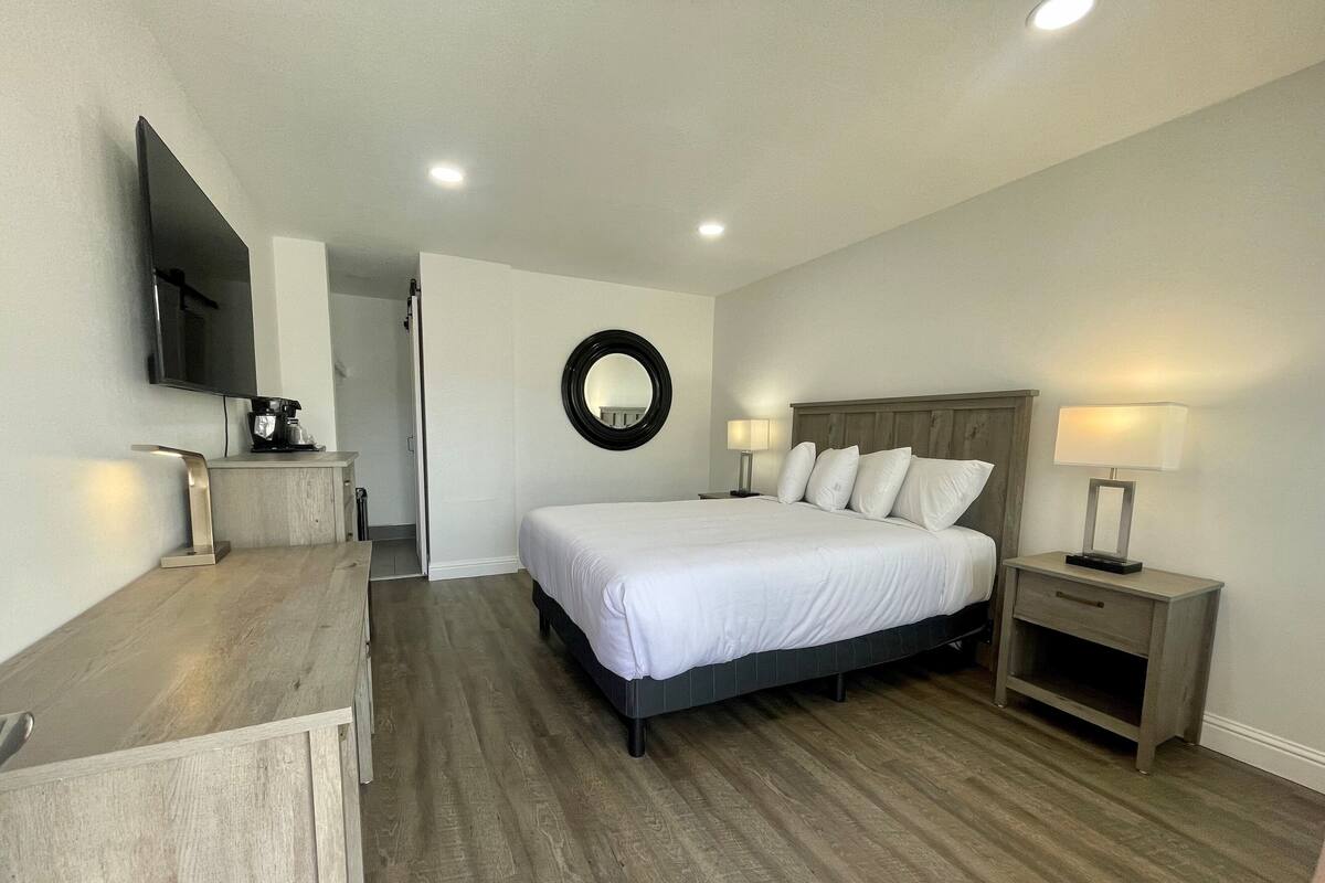 Una habitación de hotel con cama, mesitas de noche, televisión y cafetera.
