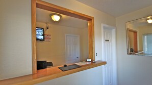 A reception area with a wooden counter, a large mirror, a television mounted on the wall, and a door in the background. - Budget Inn Lompoc (Lompoc)