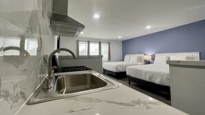 A modern kitchen with a stainless steel sink and stove, two beds with white bedding, and a blue accent wall. - Budget Inn Lompoc (Lompoc)