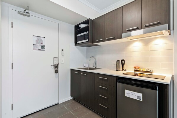 A modern kitchen with dark cabinetry, a built-in microwave, a stainless steel sink, and a dishwasher.