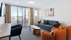 Una habitación de hotel moderna con sofá, sillas, una mesita y un balcón con cortinas.