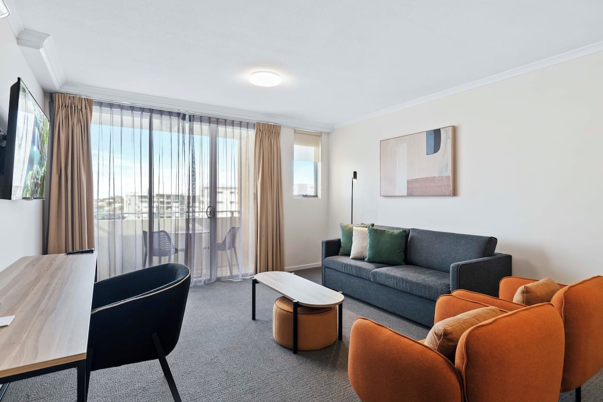A modern hotel room with a sofa, chairs, a small table, and a balcony with curtains.