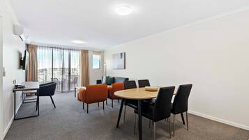 A modern hotel room with a dining area, a sofa, and a large window with curtains.