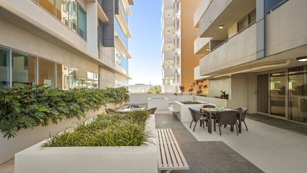 Un patio exterior moderno con mobiliario y macetas, rodeado de edificios de varios pisos.