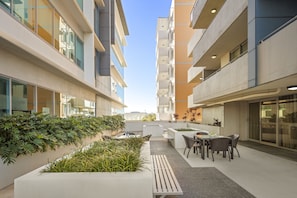 A modern outdoor patio area with seating and planters, surrounded by multi-story buildings.