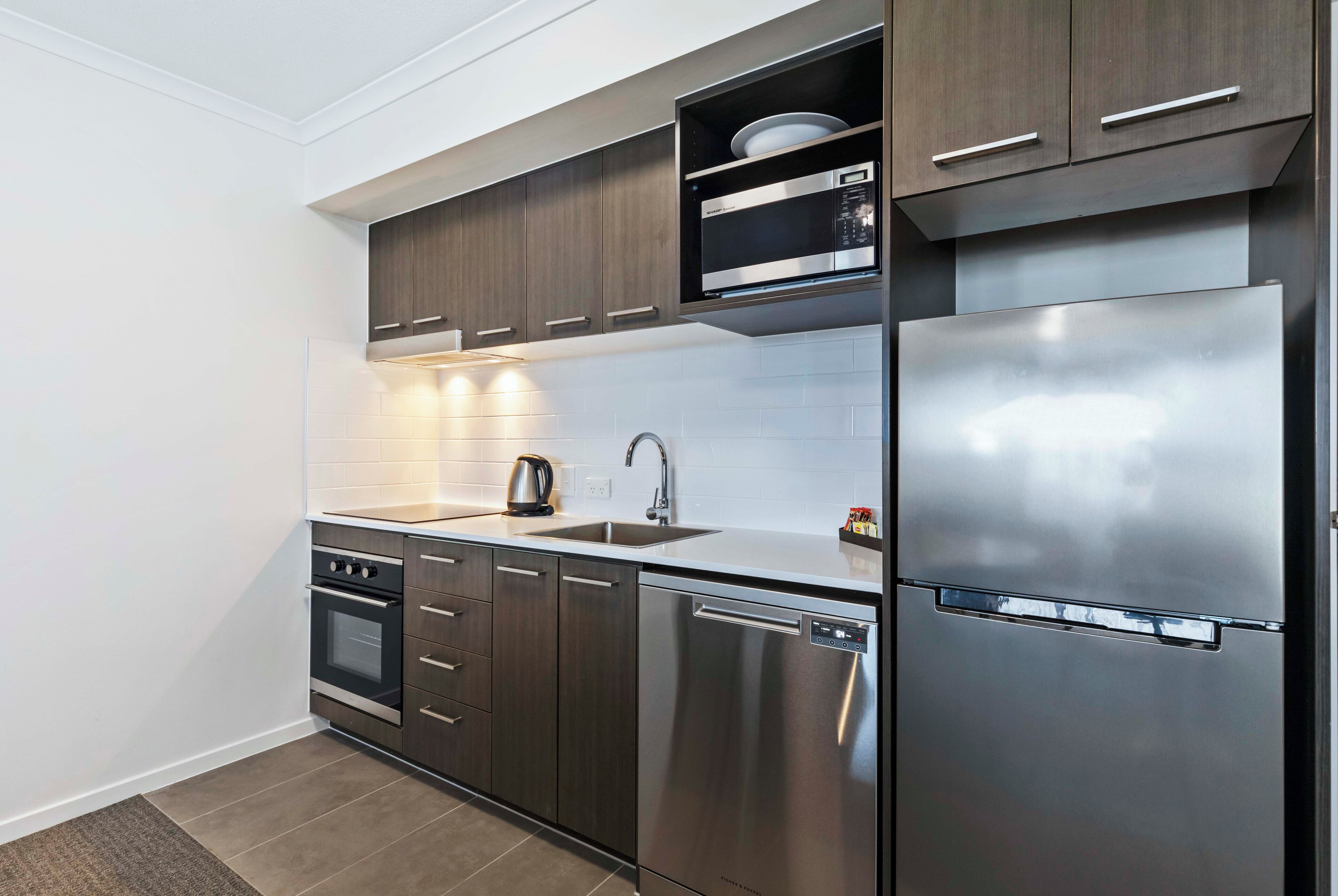 A modern kitchen with stainless steel appliances, wooden cabinets, and a built-in microwave shelf.