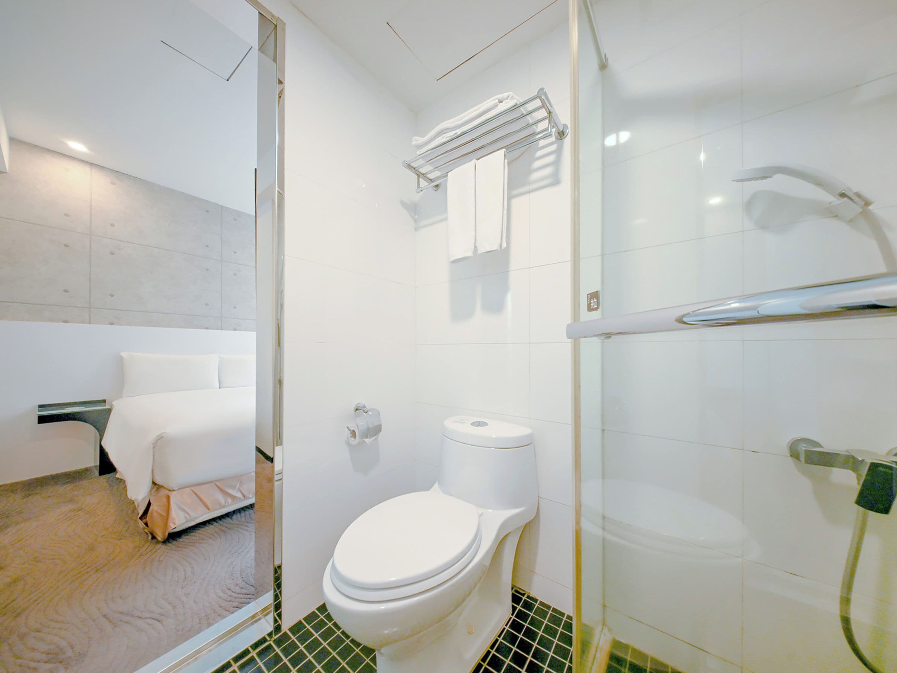 A modern bathroom with a toilet, a glass shower enclosure, and a bed with a white headboard.