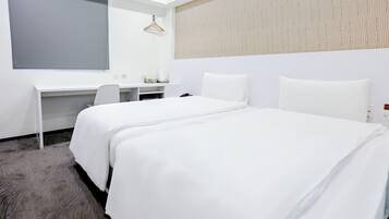 Ein Hotelzimmer mit Bett, Schreibtisch, Stuhl, Kleiderhaken und einem großen Fenster.