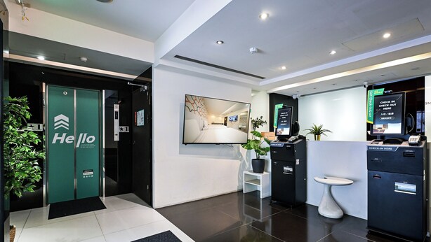 A modern hotel lobby with a reception desk, a digital check-in kiosk, a mirror, and a potted plant. - CHECK inn Express Taipei YongKang (Taipei)