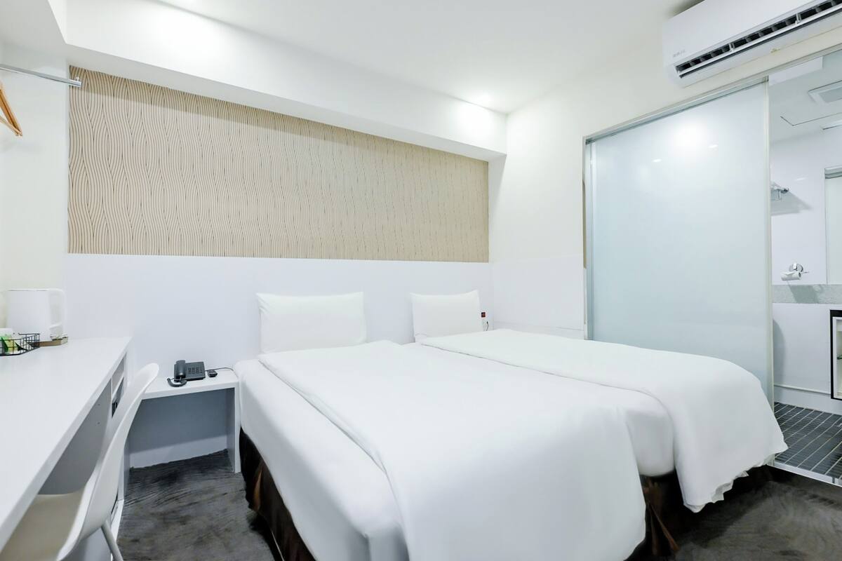 A modern hotel room with a large bed, a desk, and a wardrobe.