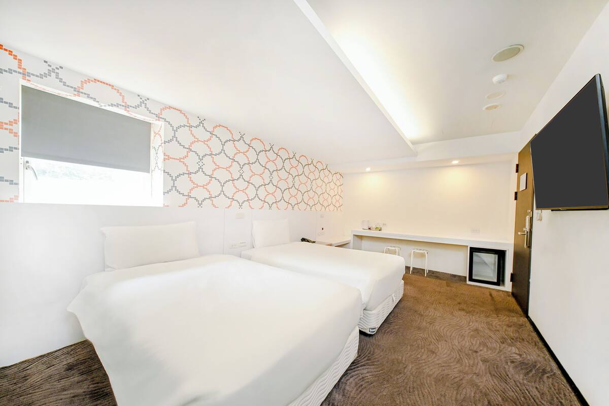 A modern hotel room with two beds, a desk, a chair, a TV, and a unique wall art.