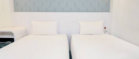 Habitación doble con dos camas, cabecero con estampado y enchufe de pared.