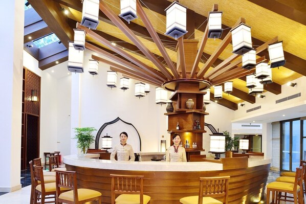 A lobby with a central reception desk, wooden chairs, and a modern chandelier.